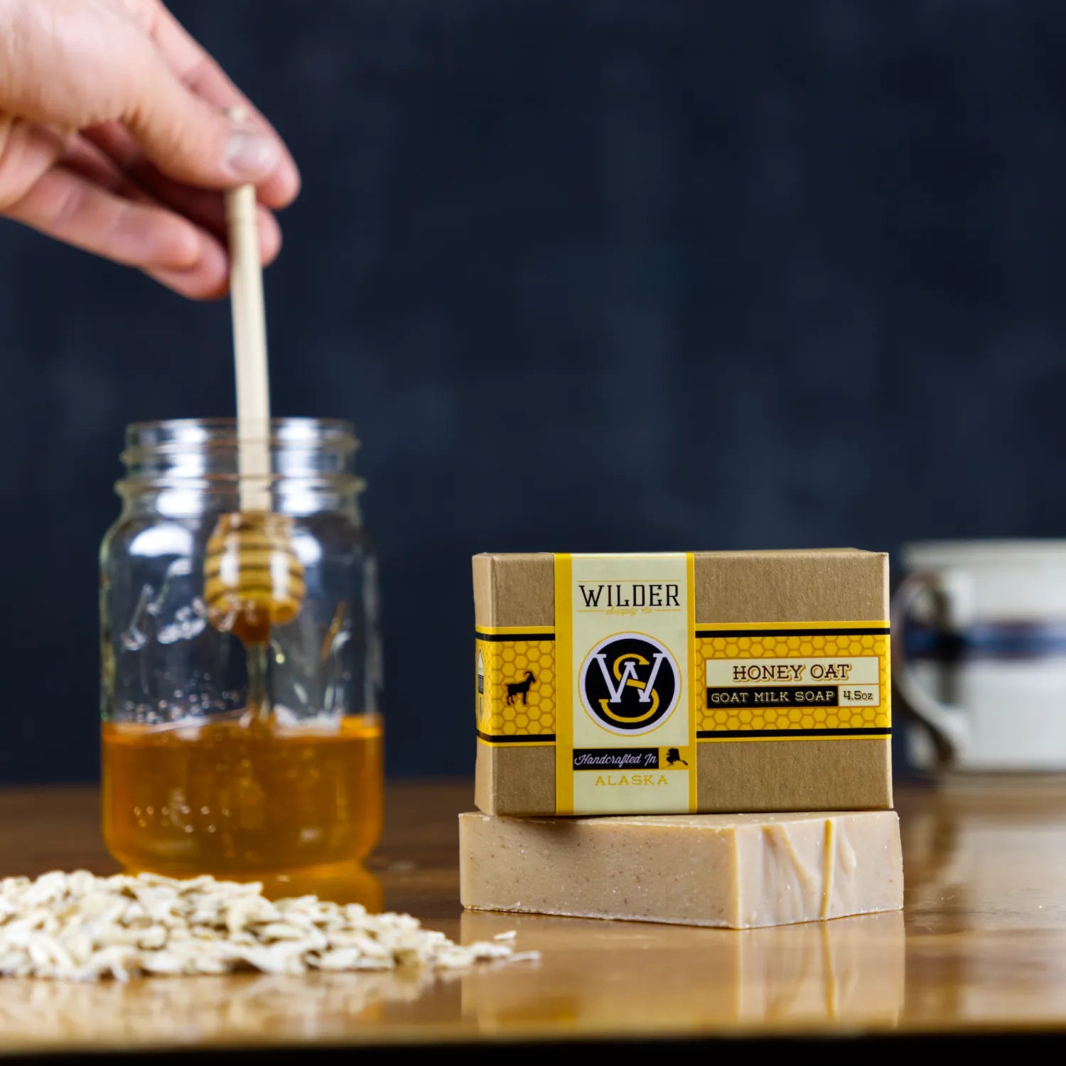 man holding wood honey dipper next to fresh rolled oats and a bar of goat milk soap