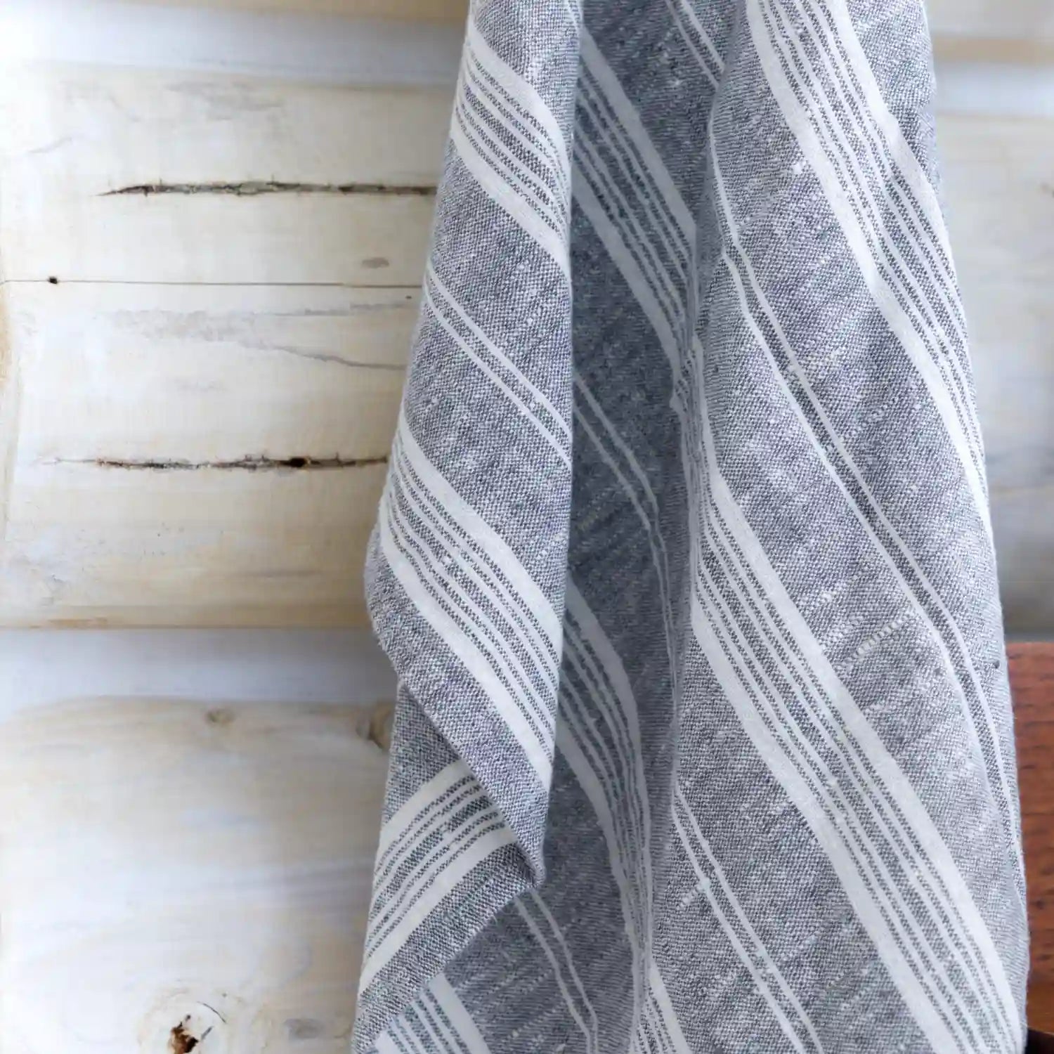 grey and white flax linen hand towel hanging on log wall.