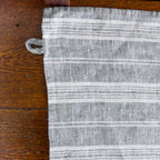 grey and white stripe flax linen hand towel laying flat on wood table.