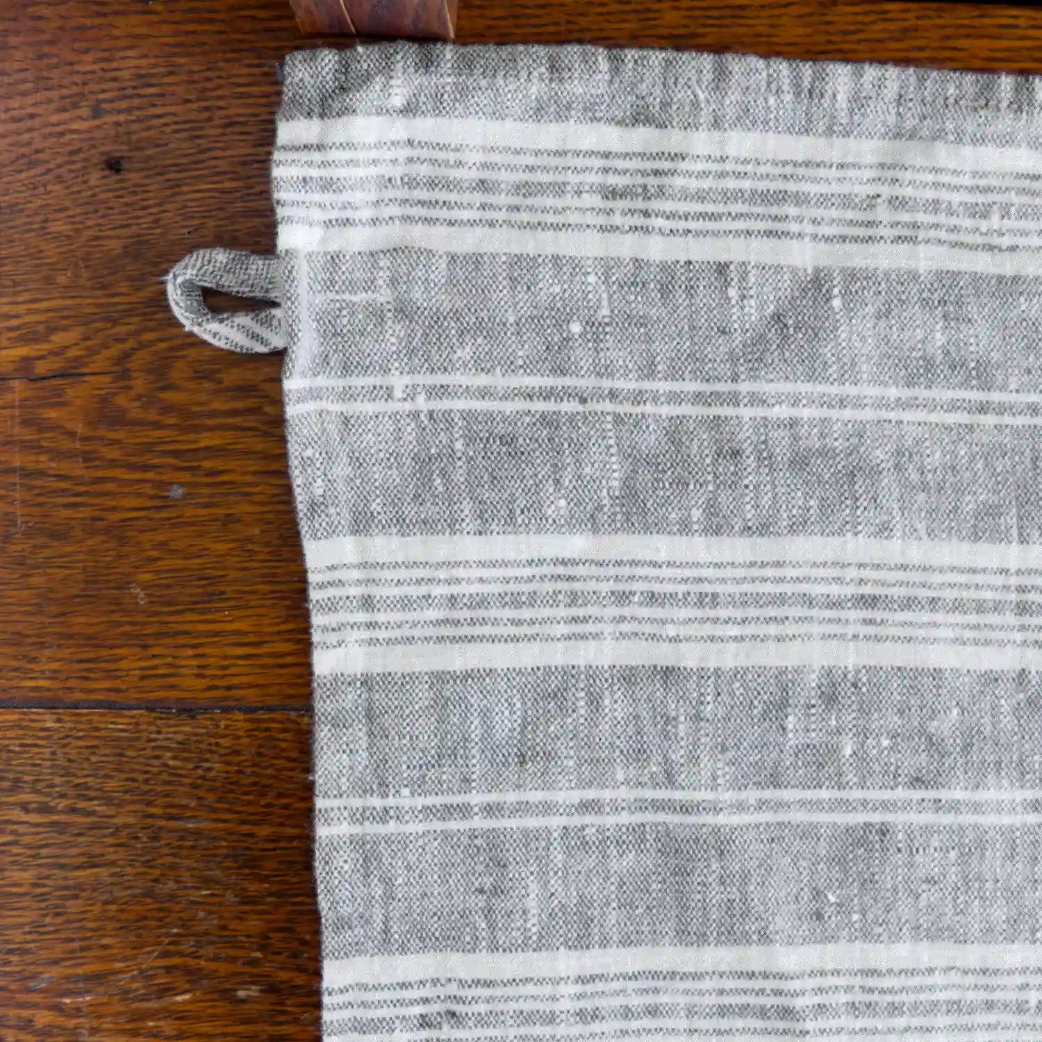 grey and white stripe flax linen hand towel laying flat on wood table.