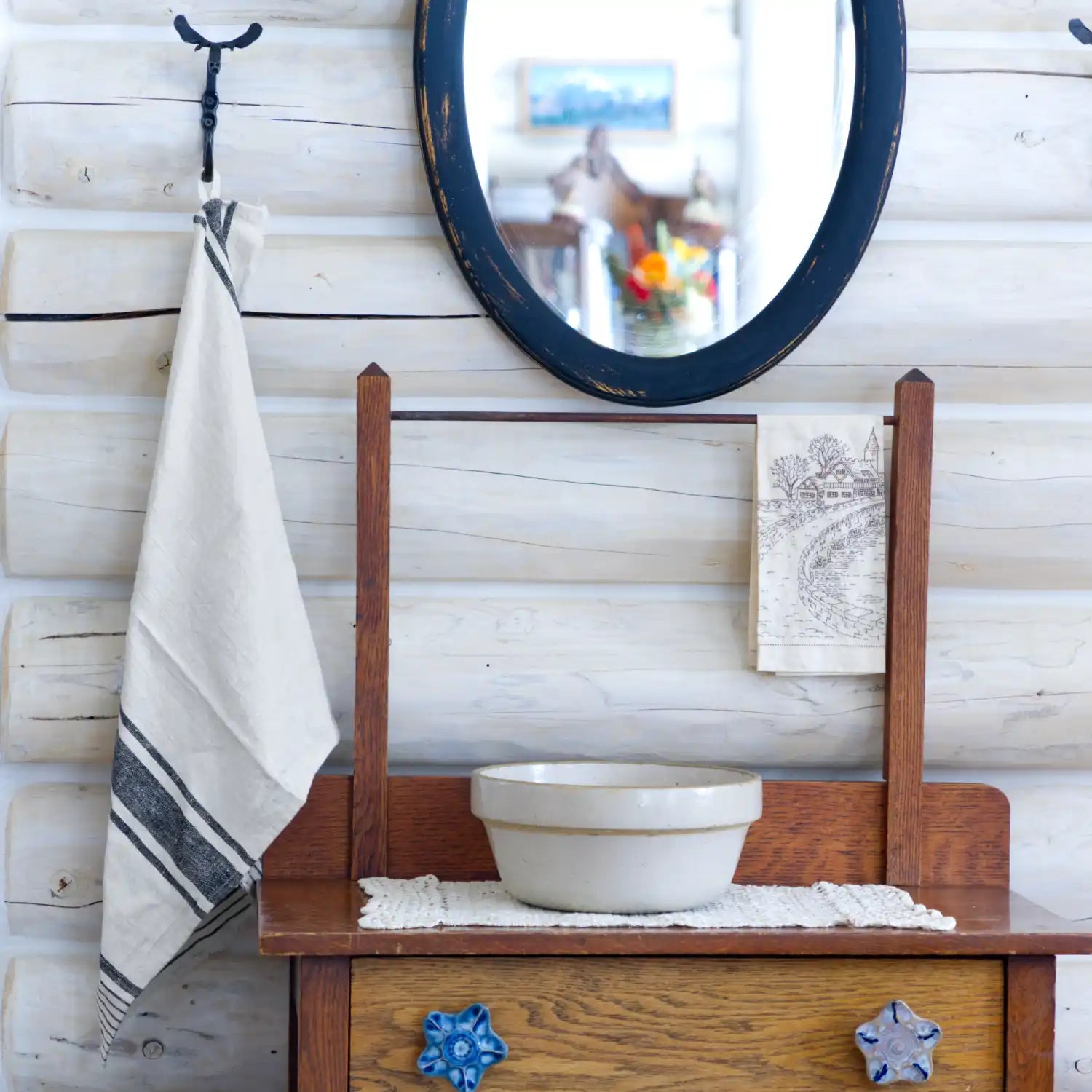 white striped flax linen hand towel hanging from blacksmith hook in log house with a mirror and washstand beside.