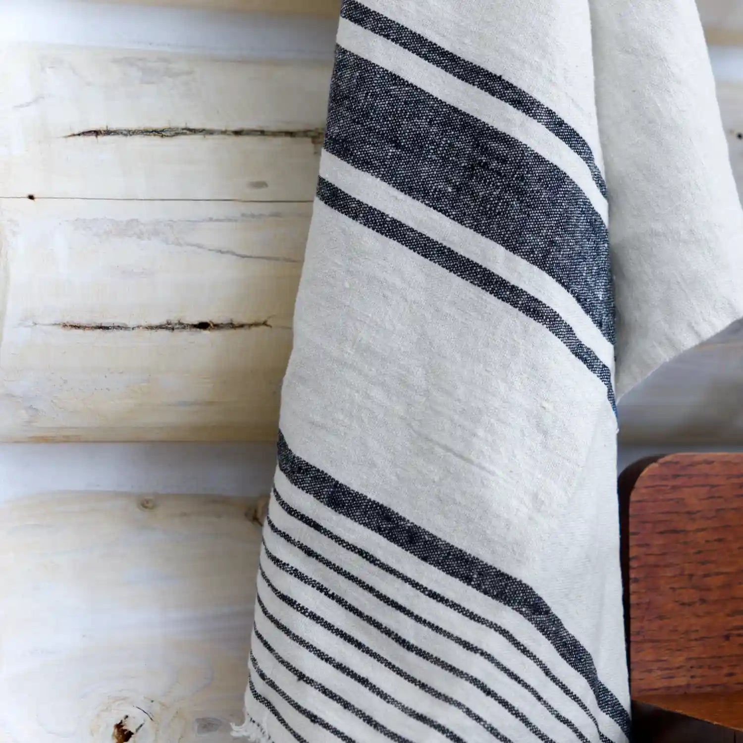 Antique white with black stripe flax linen hand towel hanging on log wall.