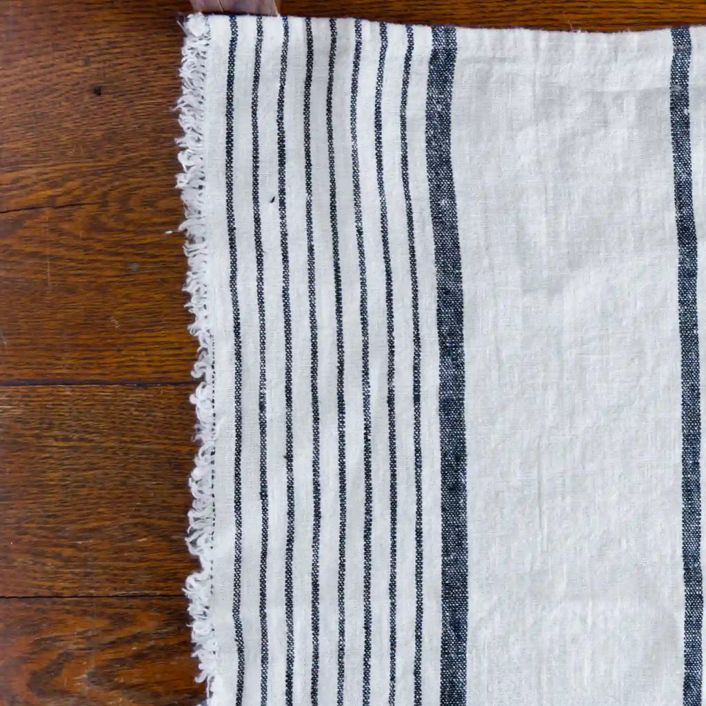 Antique white and black stripe flax linen hand towel laying flat on wood table.