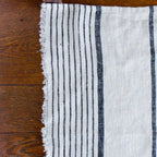 Antique white and black stripe flax linen hand towel laying flat on wood table.