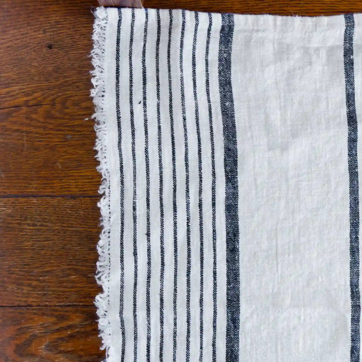 Antique white and black stripe flax linen hand towel laying flat on wood table.