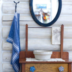 Blue and white striped flax linen hand towel hanging from blacksmith hook in log house with a mirror and washstand beside.