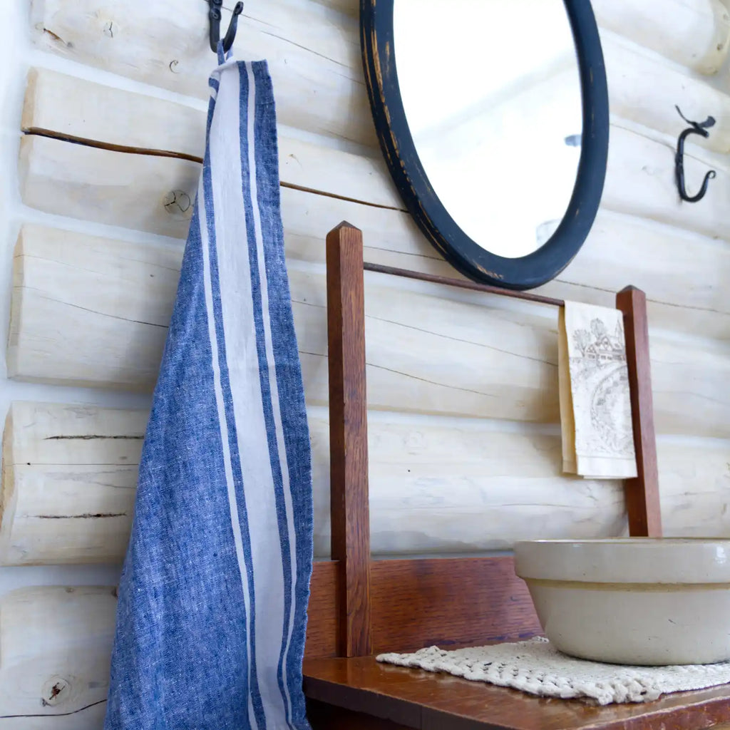 Blue and white stripe flax linen hand towel hanging from metal hook in log house