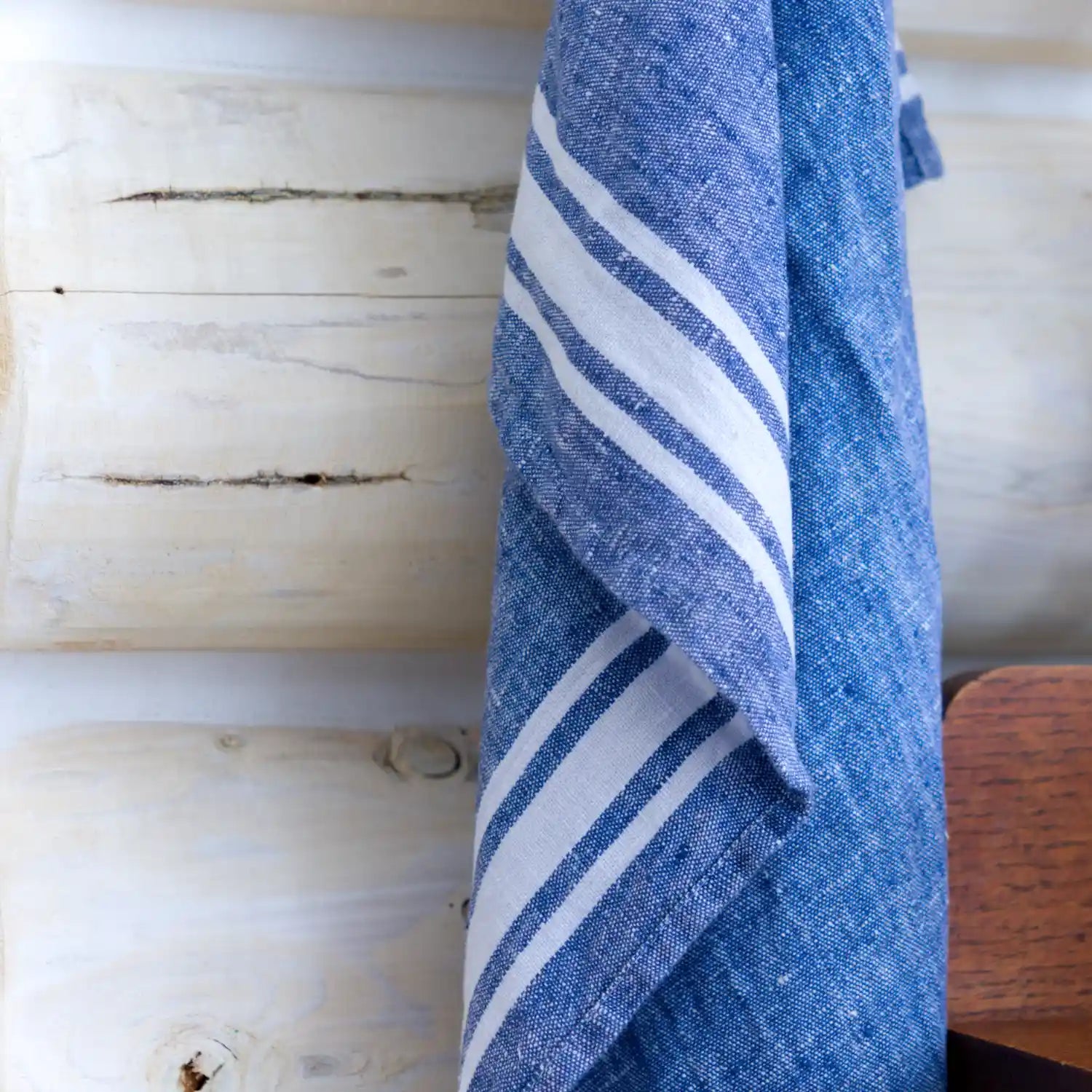 Blue with white stripe flax linen hand towel hanging on log wall.