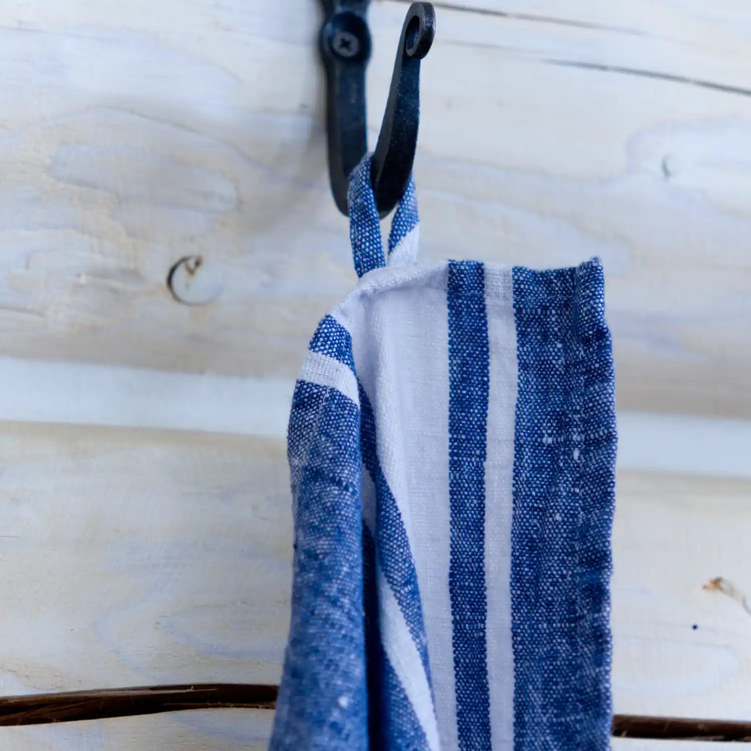 Blue and white stripe flax linen hand towel hanging from hook.
