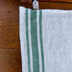 grey and green stripe flax linen hand towel laying flat on wood table.