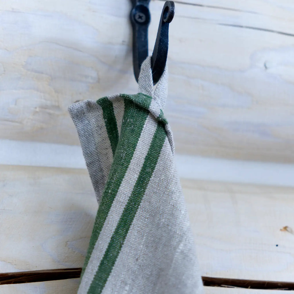 Grey and green stripe flax linen hand towel hanging from hook.