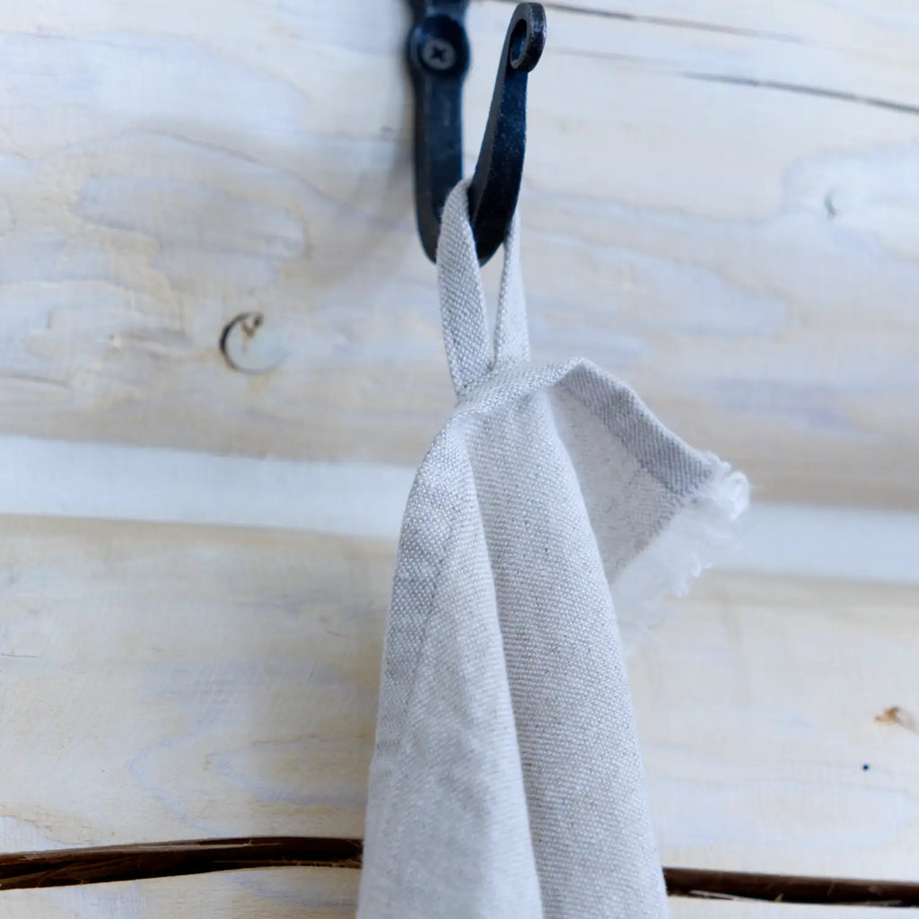 light natural frayed edge linen hand towel. Made form 100% flax. hanging on wall from metal hook in log house.