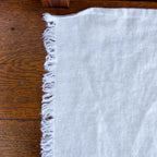 light natural frayed edge linen hand towel laying flat on wood table. made from 100% flax grown in Europe.