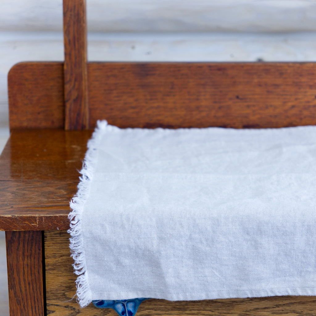 Light natural frayed edge linen hand towel laying flat on wood cabinet. made from 100% flax grown in Europe.